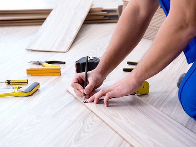 Ouvrier qui trace au crayon sur un morceau de parquet